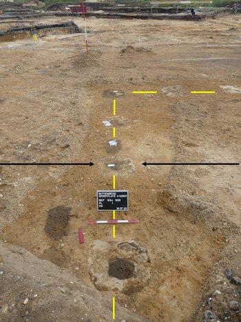 Abbildung 5: Die einzelnen Pfostenstellungen ergeben die Bauflucht (gelbe Linie) im Bereich der Nord-West-Ecke der Baracke. Die schwarzen Pfeile zeigen auf den Fundpunkt der Ikone (Befund 592). Innerhalb der Pfostengruben sind die Standspuren der Stützen als dunkle bzw. helle Flecken zu erkennen. Blick nach Norden. © Landesamt für Denkmalpflege und Archäologie Sachsen-Anhalt, Helge Jarecki. 