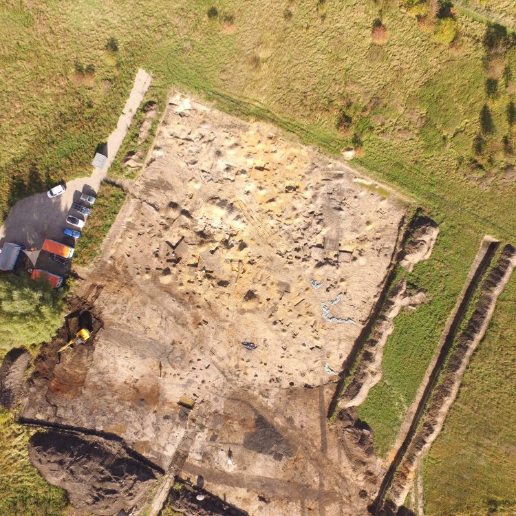 Luftaufnahme der Grabungsfläche. Im Norden (im Bild oben) sind bereits weitgehend ausgegrabene Siedlungsbefunde auf der Sandterrasse an der Ohre zu sehen. Im Süden ist der hochmittelalterliche Befestigungsgraben als dunkler, am Rand der Grabungsfläche von Westen nach Osten verlaufender Streifen zu erkennen. © Landesamt für Denkmalpflege und Archäologie Sachsen-Anhalt, Bodo Hänler.