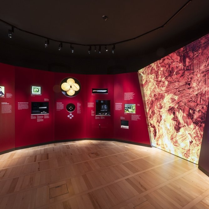 Ausstellungsimpression: Blick in die Kabinettausstellung ›Klöster. Geplündert. In den Wirren der Bauernaufstände‹. Die Ausstellungsbereiche zu Himmelpforte (links) und Kaltenborn (rechts) sind farblich voneinander abgesetzt. Die Zentralinstallation der von Klaus Pockrandt (Halle [Saale]) gestalteten Ausstellung zeigt einen fliehenden Mönch auf flammendem Grund. © Landesamt für Denkmalpflege und Archäologie Sachsen-Anhalt, Michel Klehm.