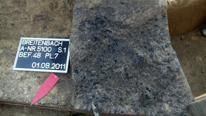 Abbildung 1a: Ausschnitt der freigelegten Holzkohleschicht mit Feuersteinfunden und einem länglichen Geröll am unteren Bildrand. © Landesamt für Denkmalpflege und Archäologie Sachsen-Anhalt, Andreas Siegl.  