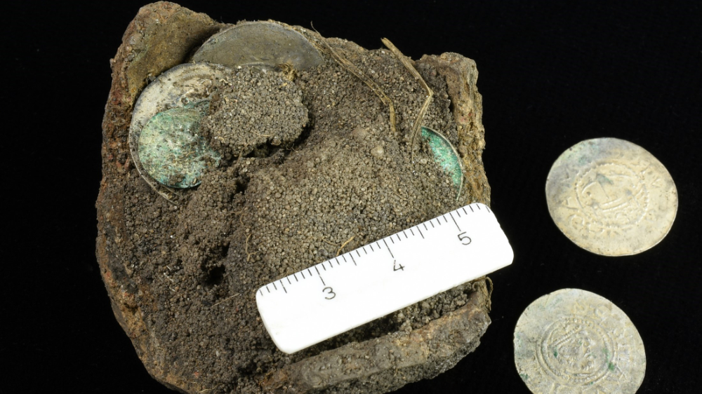 Abbildung 2: Das freigelegte Keramikgefäß mit einigen der Münzen. Die zwei silbernen Denare können in die Zeit von Erzbischof Hunfried datiert werden. © Landesamt für Denkmalpflege und Archäologie Sachsen-Anhalt, Frederike Hertel.